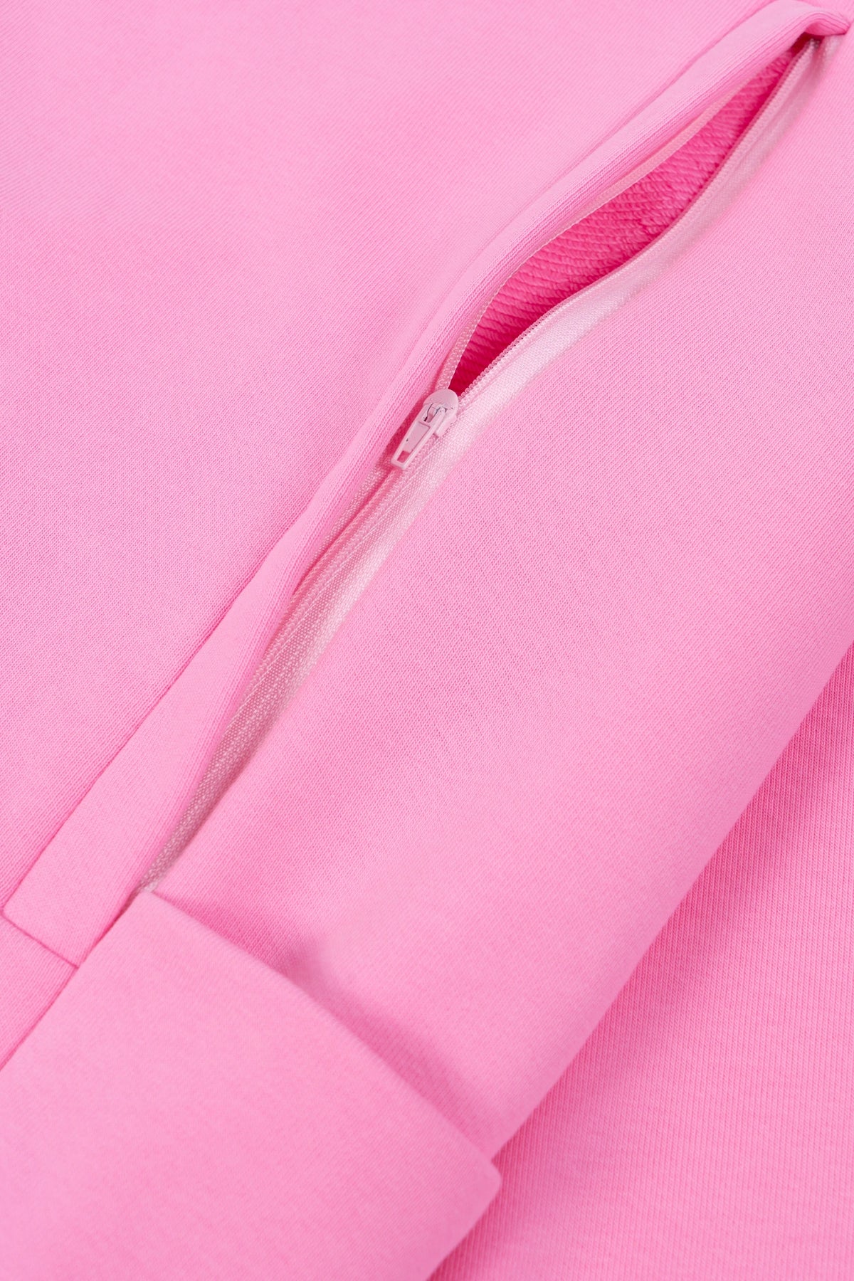 Zbliżenie na zameczki do karmienia (detal) rozłożonej na płasko różowej bluzy dresowej typu crewneck z długim rękawem, z ukrytymi panelami ułatwiającymi karmienie i haftem "no plans.".