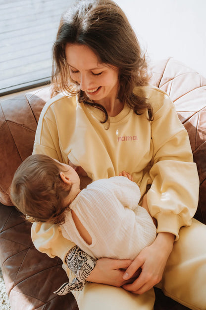 Uśmiechnięta mama w bananowej bluzie do karmienia Melanie z napisem mama. trzyma dziecko na kolanach