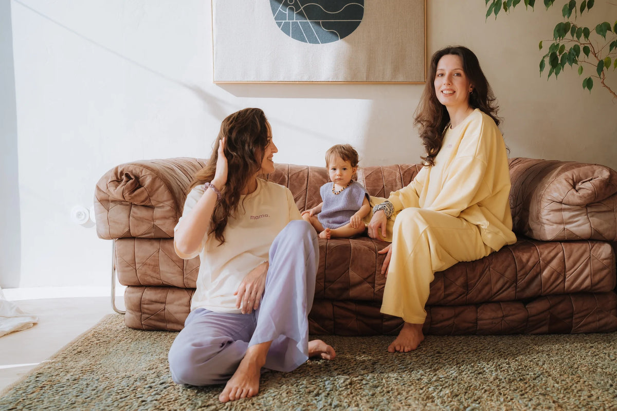 Mama w bananowej bluzie Melanie mama. siedzi na kanapie z dzieckiem, obok przyjaciółka w kremowym t-shircie