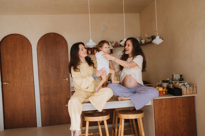 Dwie mamy, w bananowej bluzie Melanie i kremowym t-shircie mama., bawią się z dzieckiem w kuchni