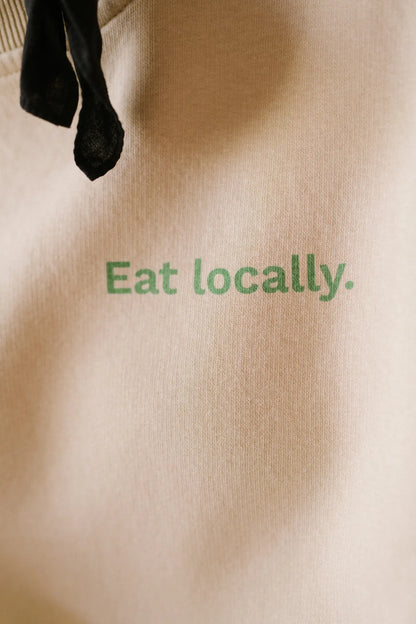 Zbliżenie na zielony nadruk Eat locally na beżowej bluzie Melanie z drapanej dzianiny