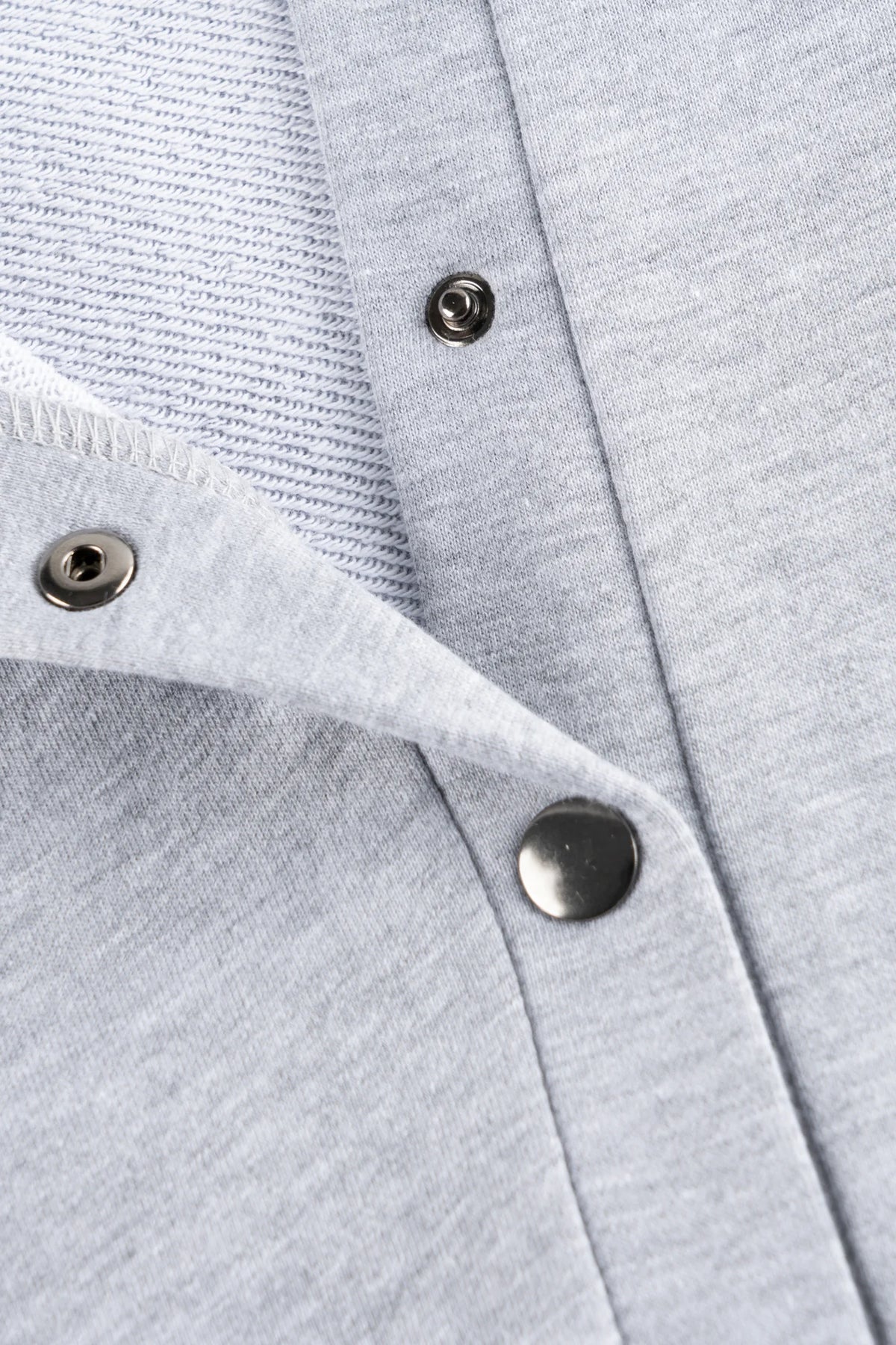 Zbliżenie na rozpięte metalowe zatrzaski szarej bluzy polo do karmienia