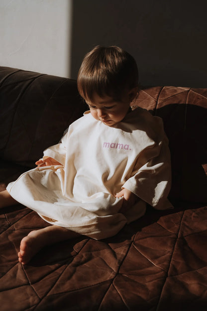 Maluch w za dużej kremowej koszulce z napisem mama. siedzący na brązowej skórzanej kanapie