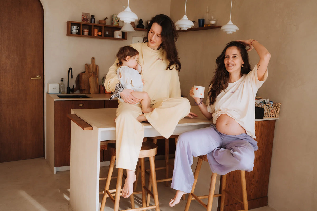 Mama w bananowych spodniach dresowych i bluzie mama. karmi dziecko, siedząc na blacie w kuchni