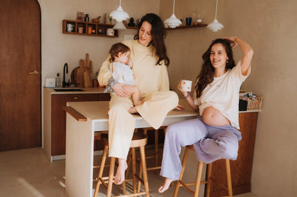 Mama w bananowych spodniach dresowych i bluzie mama. karmi dziecko, siedząc na blacie w kuchni