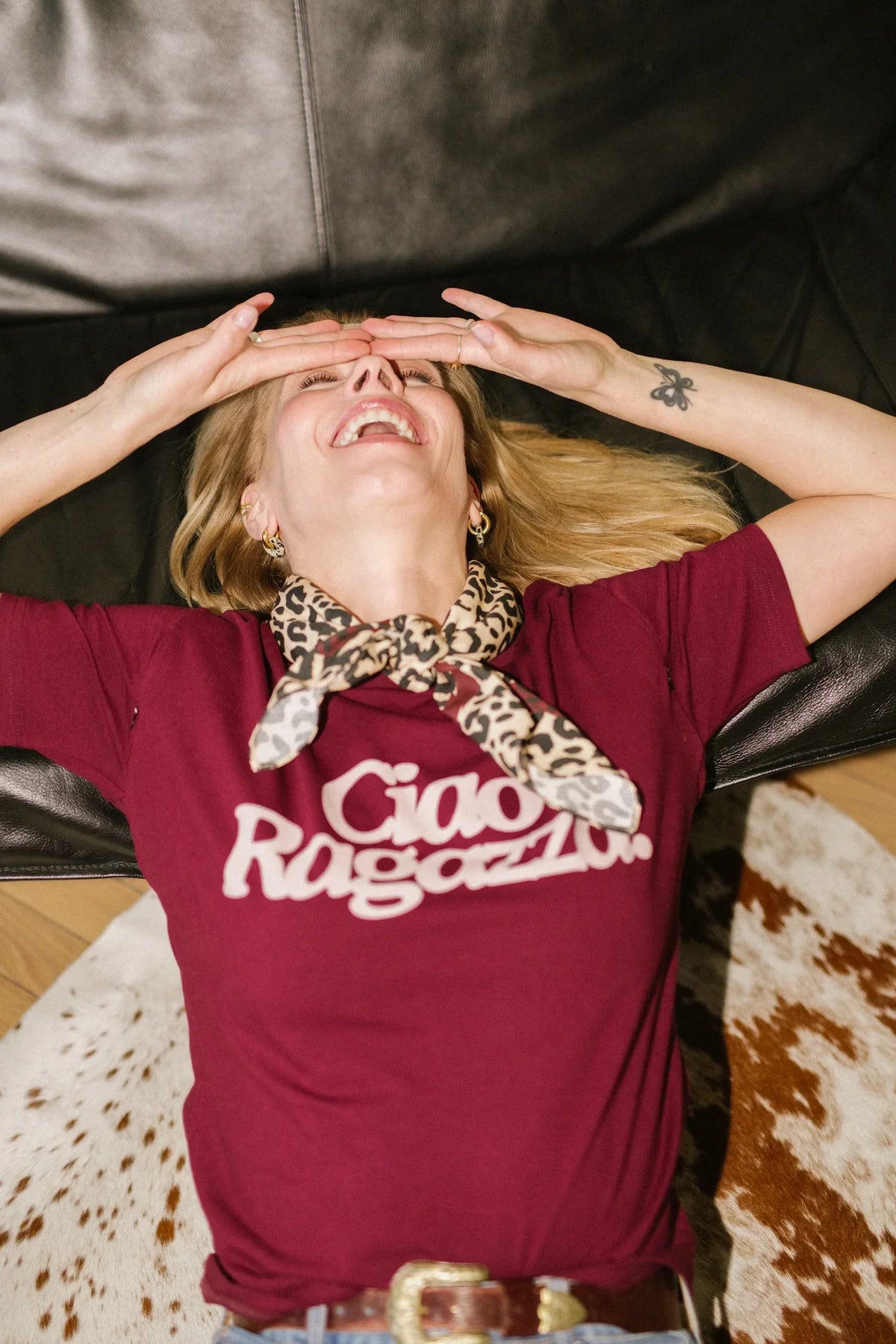 Roześmiana kobieta w winnym t-shircie Helen Ciao Ragazza i panterkowej apaszce leży na dywanie