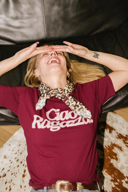 Roześmiana kobieta w winnym t-shircie Helen Ciao Ragazza i panterkowej apaszce leży na dywanie