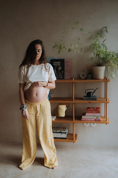 Kobieta w ciąży w kokosowym t-shircie damskim Helen i żółtych spodniach odsłania brzuszek