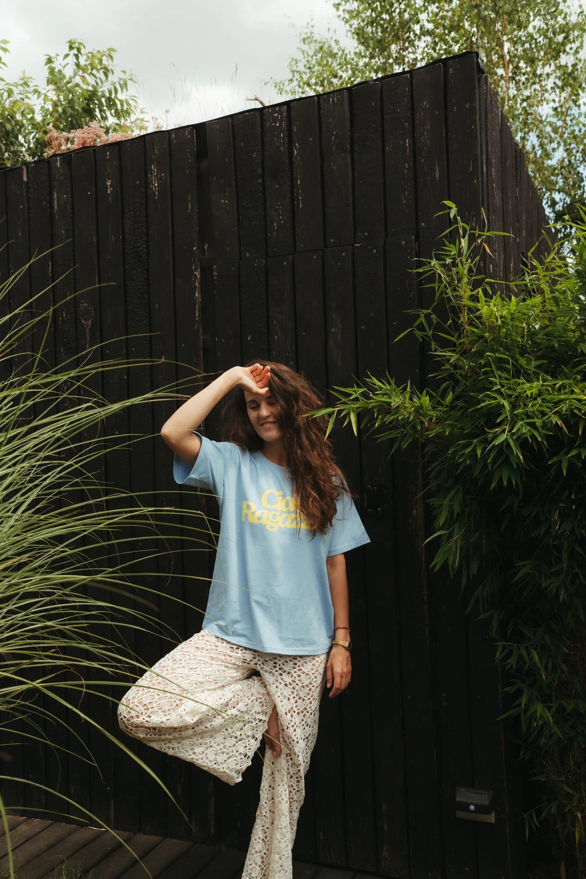 Uśmiechnięta kobieta w niebieskim t-shircie damskim oversize Ciao Ragazza i koronkowych spodniach w ogrodzie