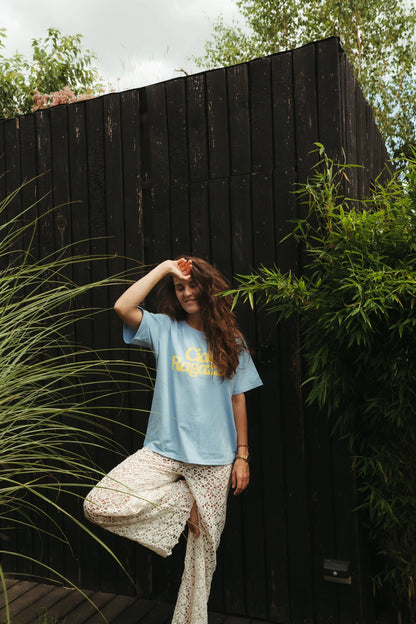 Uśmiechnięta kobieta w niebieskim t-shircie damskim oversize Ciao Ragazza i koronkowych spodniach w ogrodzie