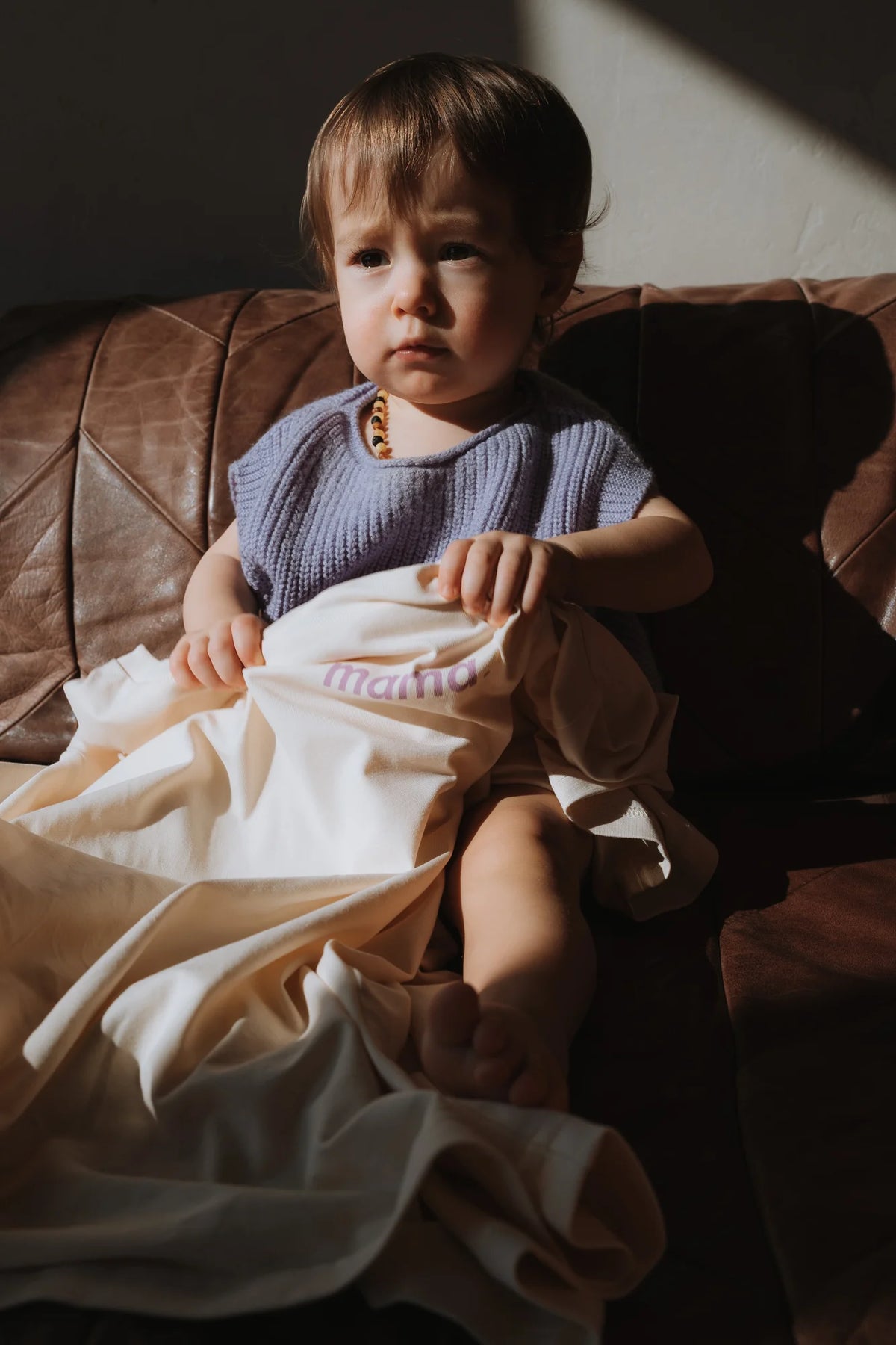 Dziecko w lawendowej kamizelce siedzi na skórzanej kanapie z kremowym t-shirtem mama. na kolanach