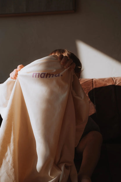 Dziecko chowa się pod kremowym t-shirtem oversize z napisem mama. na brązowej kanapie