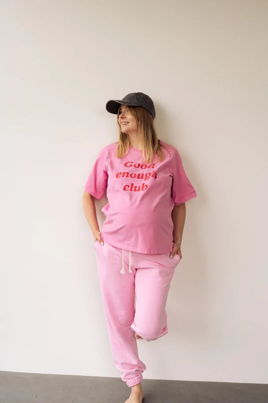 Uśmiechnięta kobieta w ciąży w różowym t-shircie do karmienia Good enough club i różowych spodniach dresowych