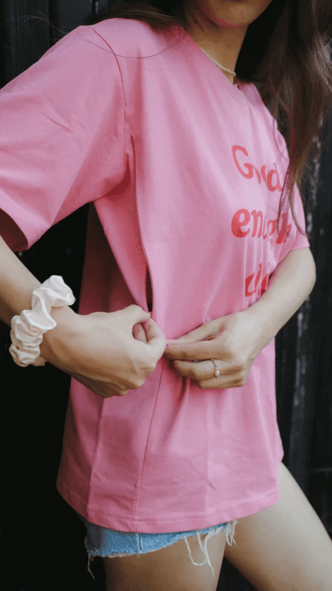 Kobieta odsłania ukryty zamek do karmienia z boku różowego t-shirtu oversize Good enough club