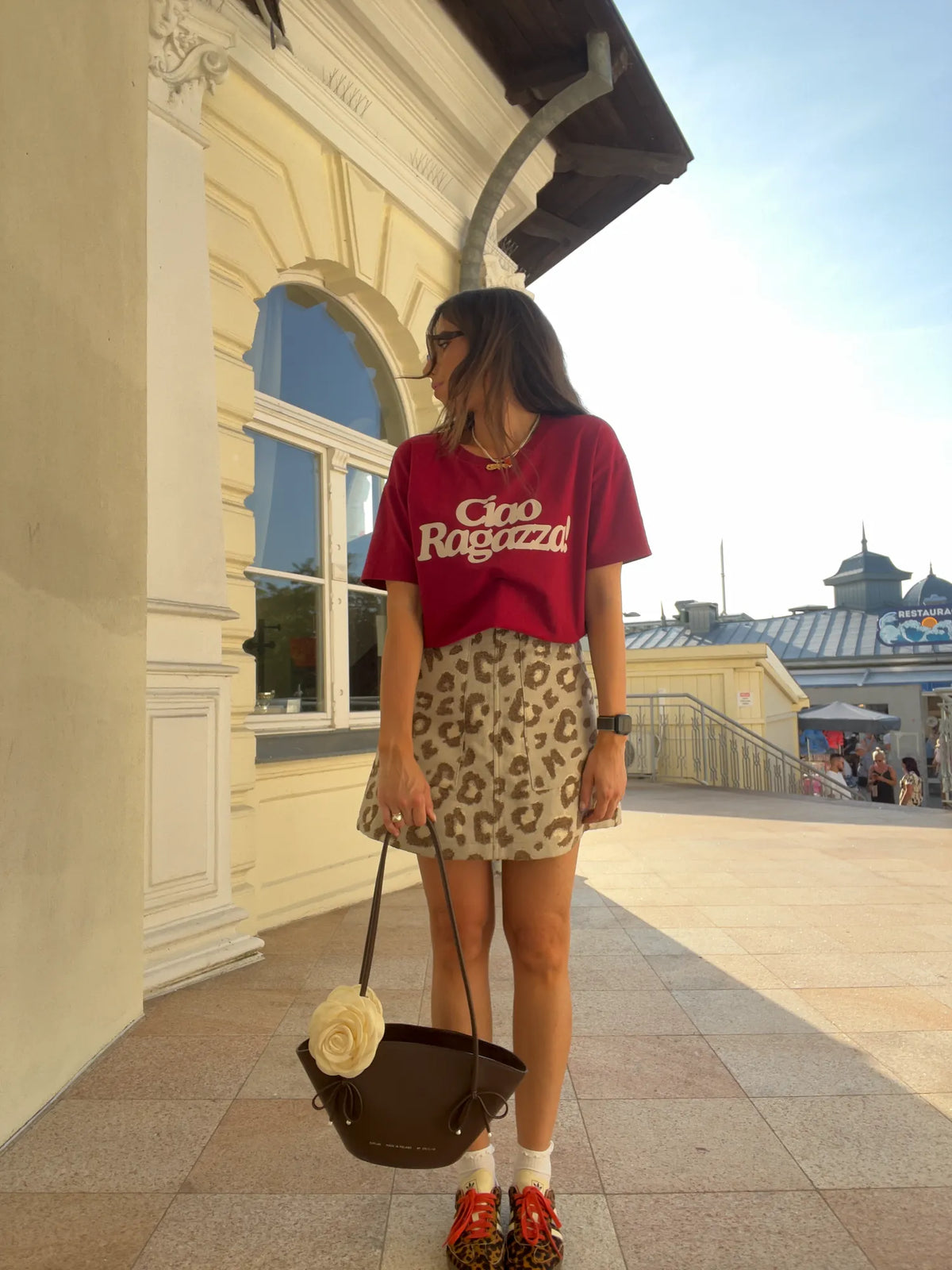 Kobieta w bordowym t-shircie Helen z białym napisem Ciao Ragazza, zestawionym z panterkową spódnicą i brązową torebką